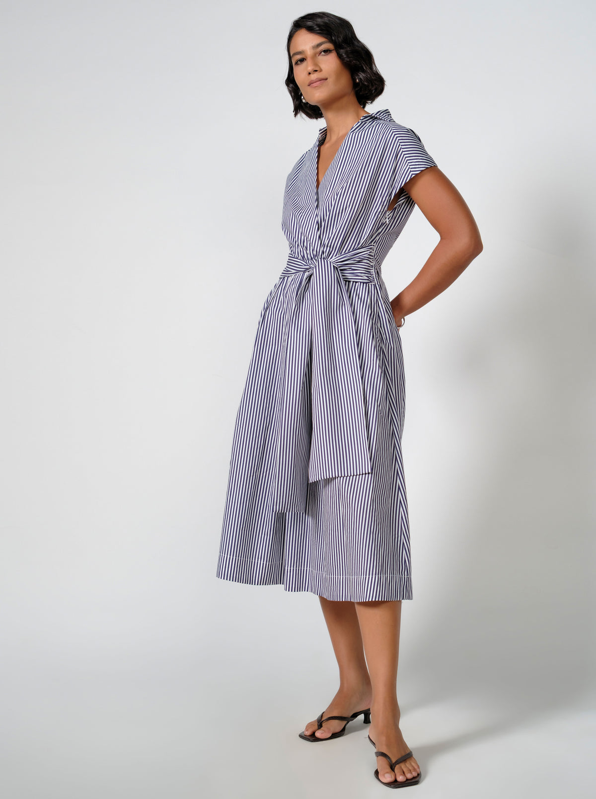 Woman wearing the Arienti Jane Striped Tie Waist Midi Dress in navy, side view